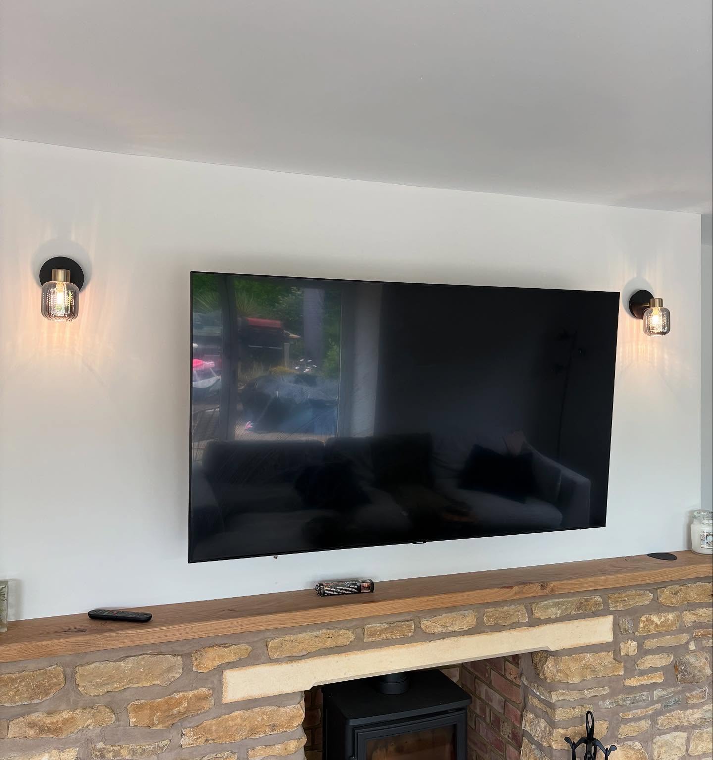 Wall lights and a wall mounted television supplied above a stone fireplace