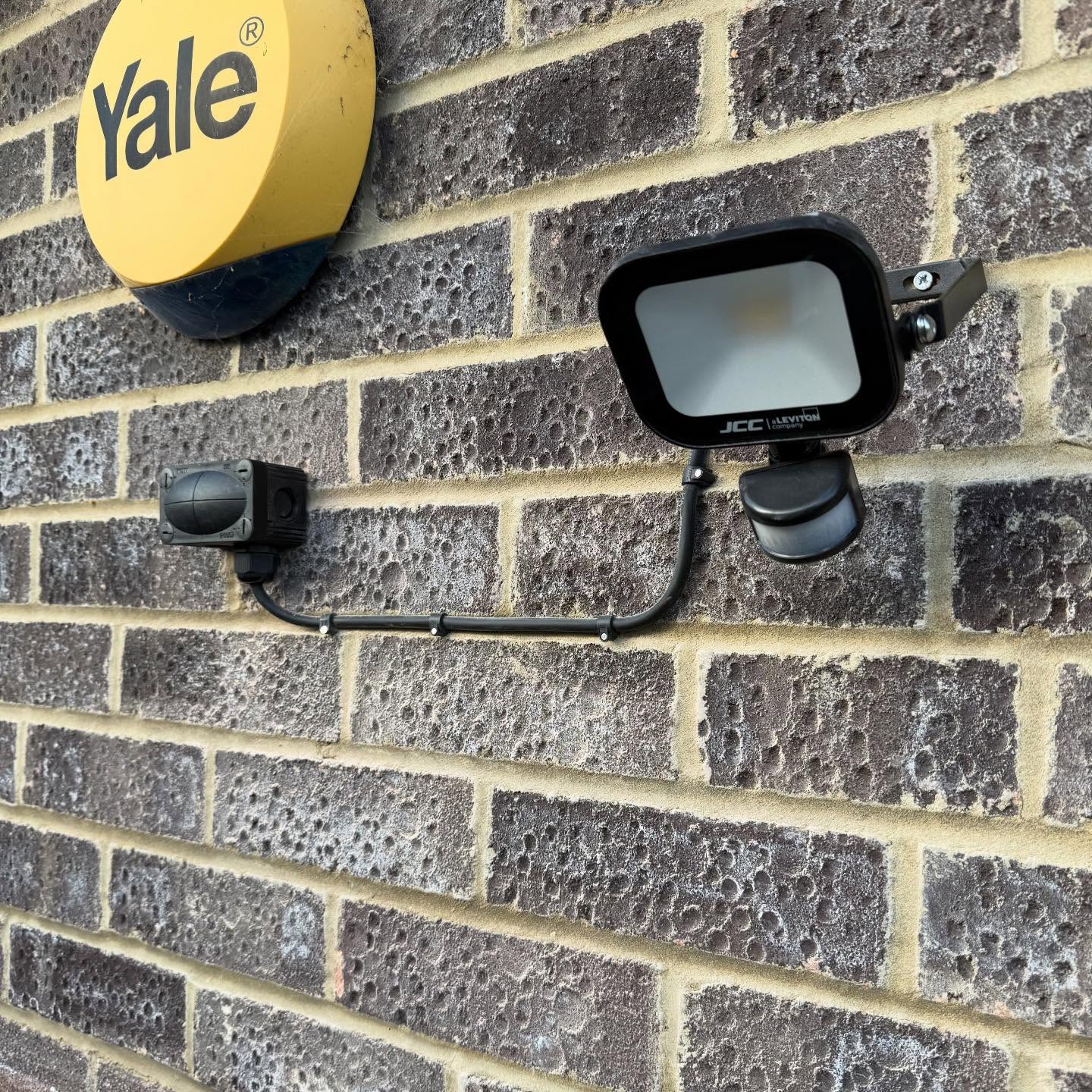 PIR security floodlight installed beside an alarm box on a house exterior