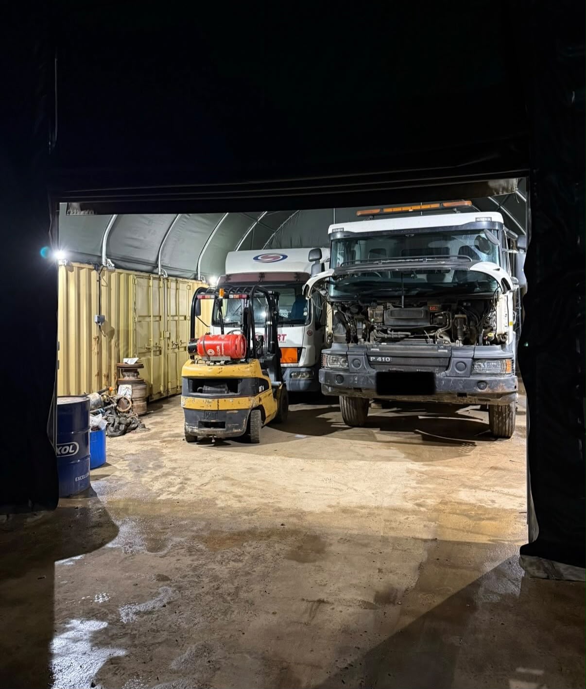 Lit canopy structure over lorries and a forklift at a Northamptonshire rural business park at night